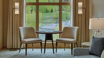 Habitación de hotel con un ventanal grande, dos sillones, una mesa redonda, un sofá y una lámpara.