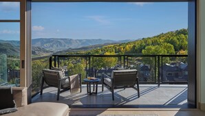 Varanda com vista para montanhas e árvores, equipada com cadeiras e uma mesa.