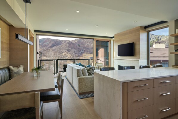 Una cocina moderna con una isla grande, un comedor con vistas a las montañas y un televisor de pantalla plana montado en la pared.