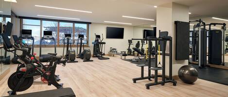 Ett gym med konditionsmaskiner, styrketräningsutrustning och en stor spegel.