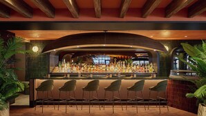 Uma área de bar com teto de madeira curvo, diversos frascos nas prateleiras e vários bancos altos.