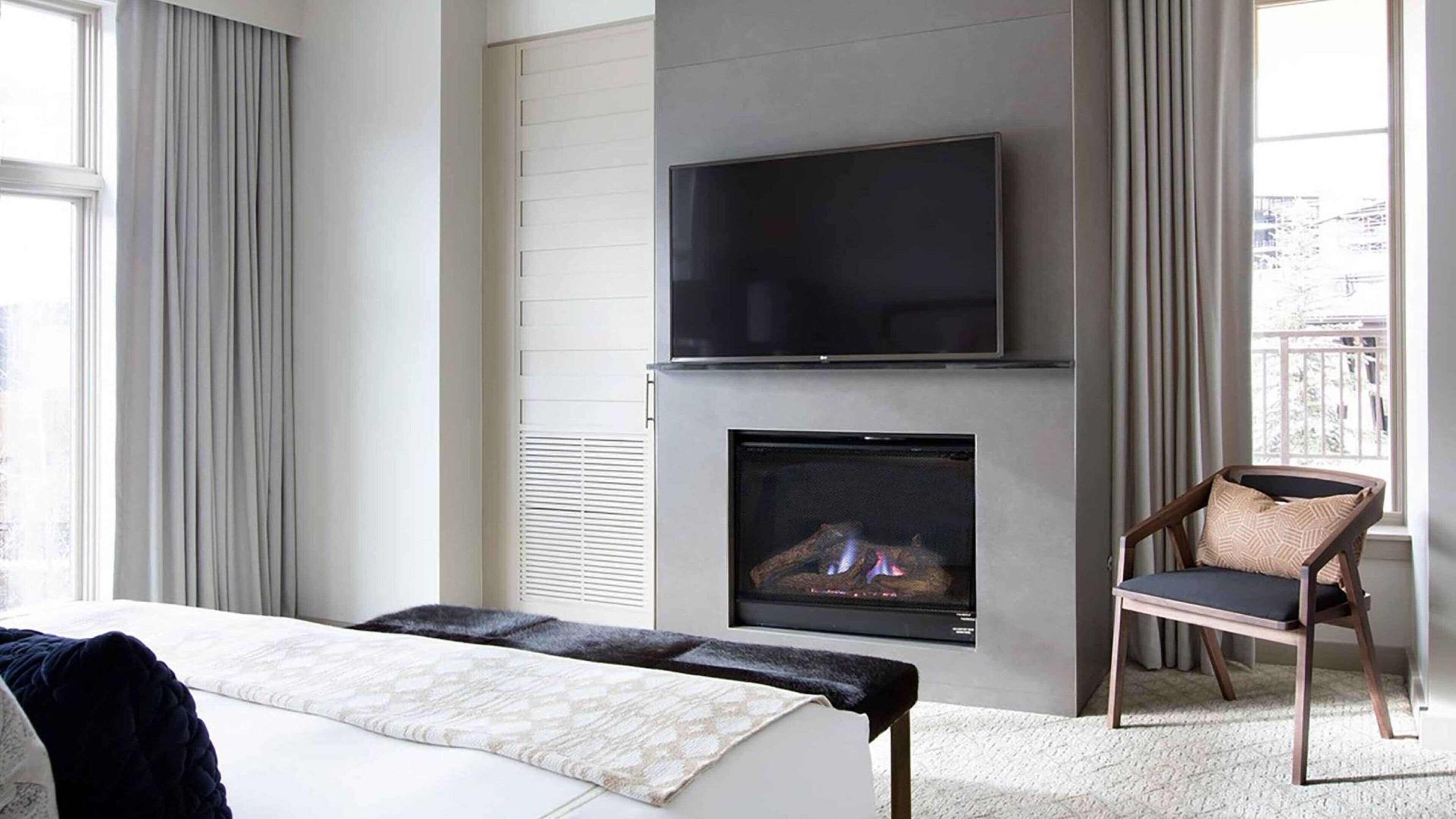 Ein modernes Hotelzimmer mit einem großen Bett, einem Flachbildfernseher über einem Kamin und Blick auf die Stadt durch große Fenster.