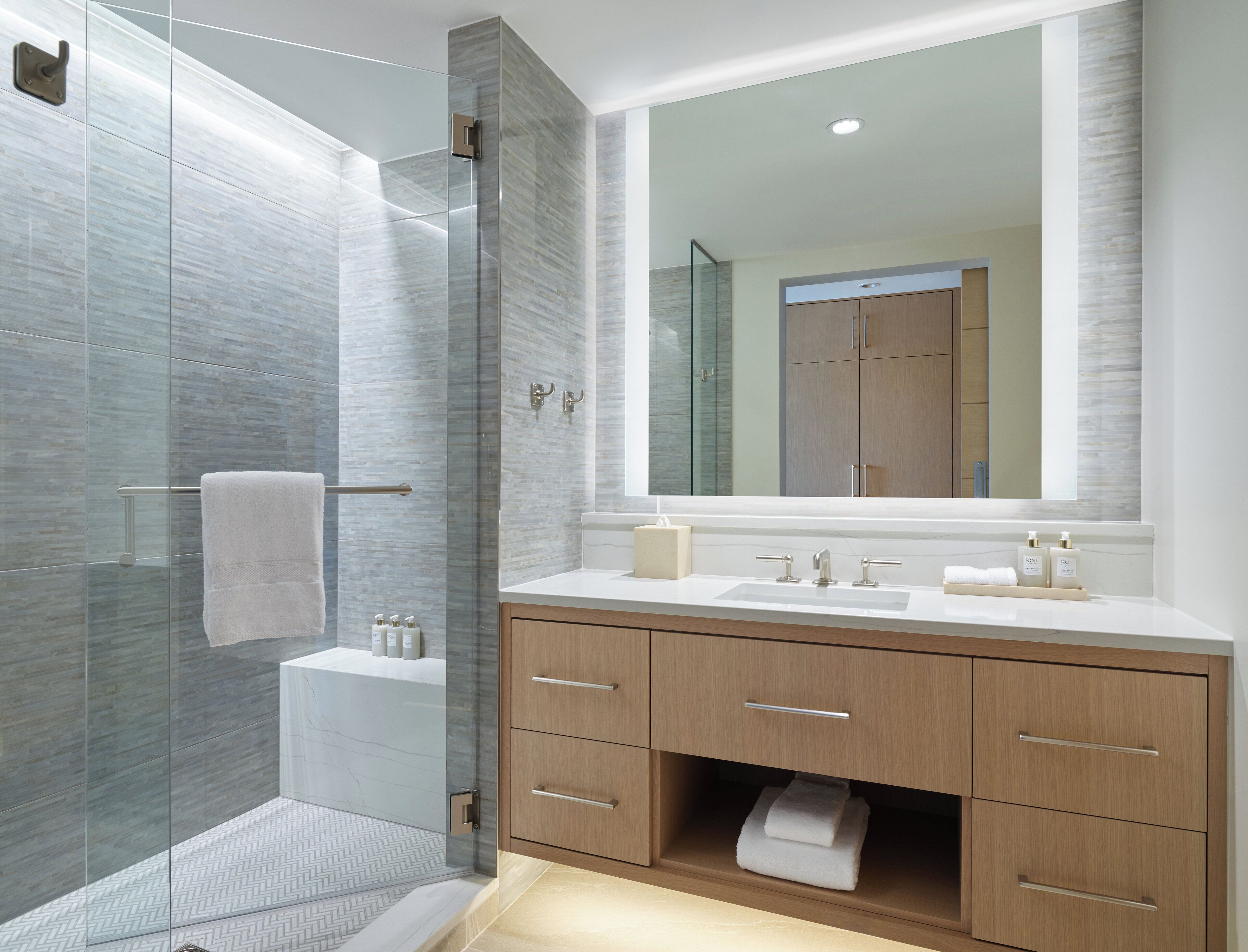 A modern bathroom with a glass shower enclosure, a large mirror, and wooden cabinets.