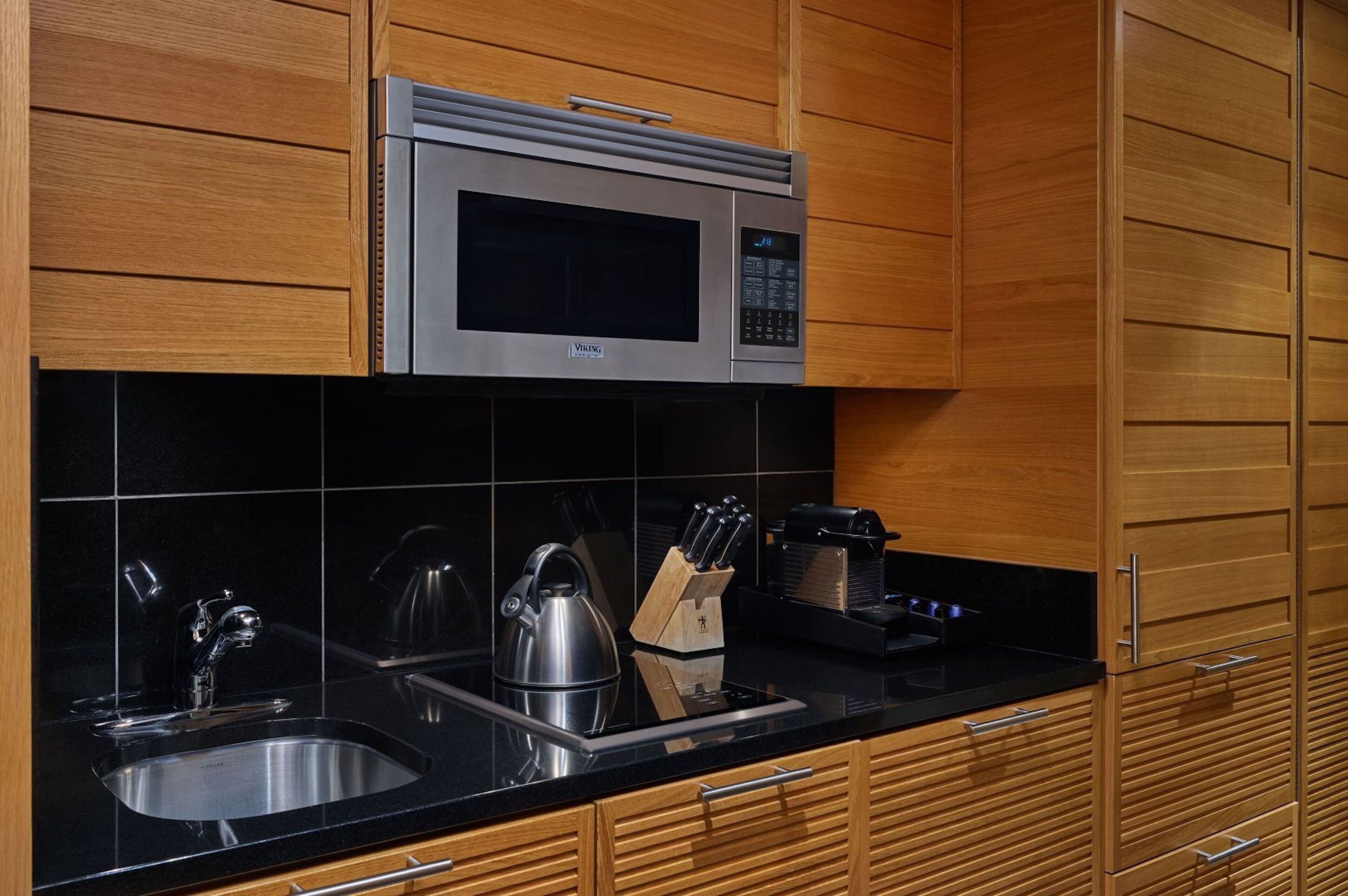 A modern kitchen with a stainless steel microwave, black countertop, and wooden cabinets.