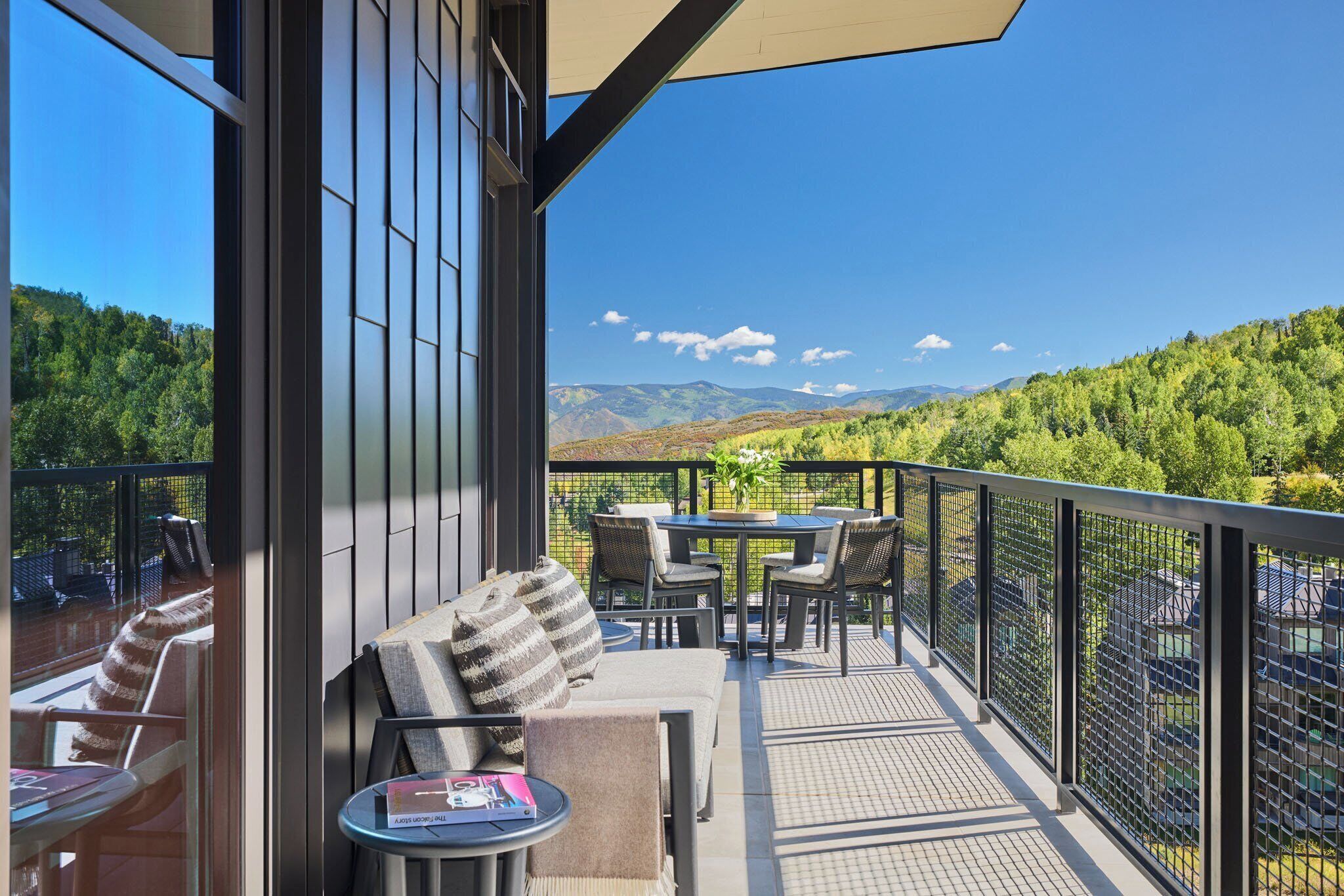 A balcony with outdoor furniture, a table, and a view of a mountainous landscape.