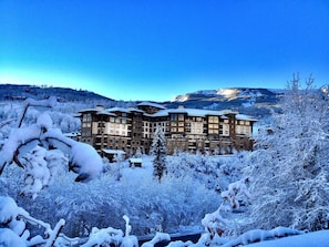Un hotel de varios pisos con una fachada simétrica, rodeado de árboles cubiertos de nieve y un paisaje montañoso de fondo.