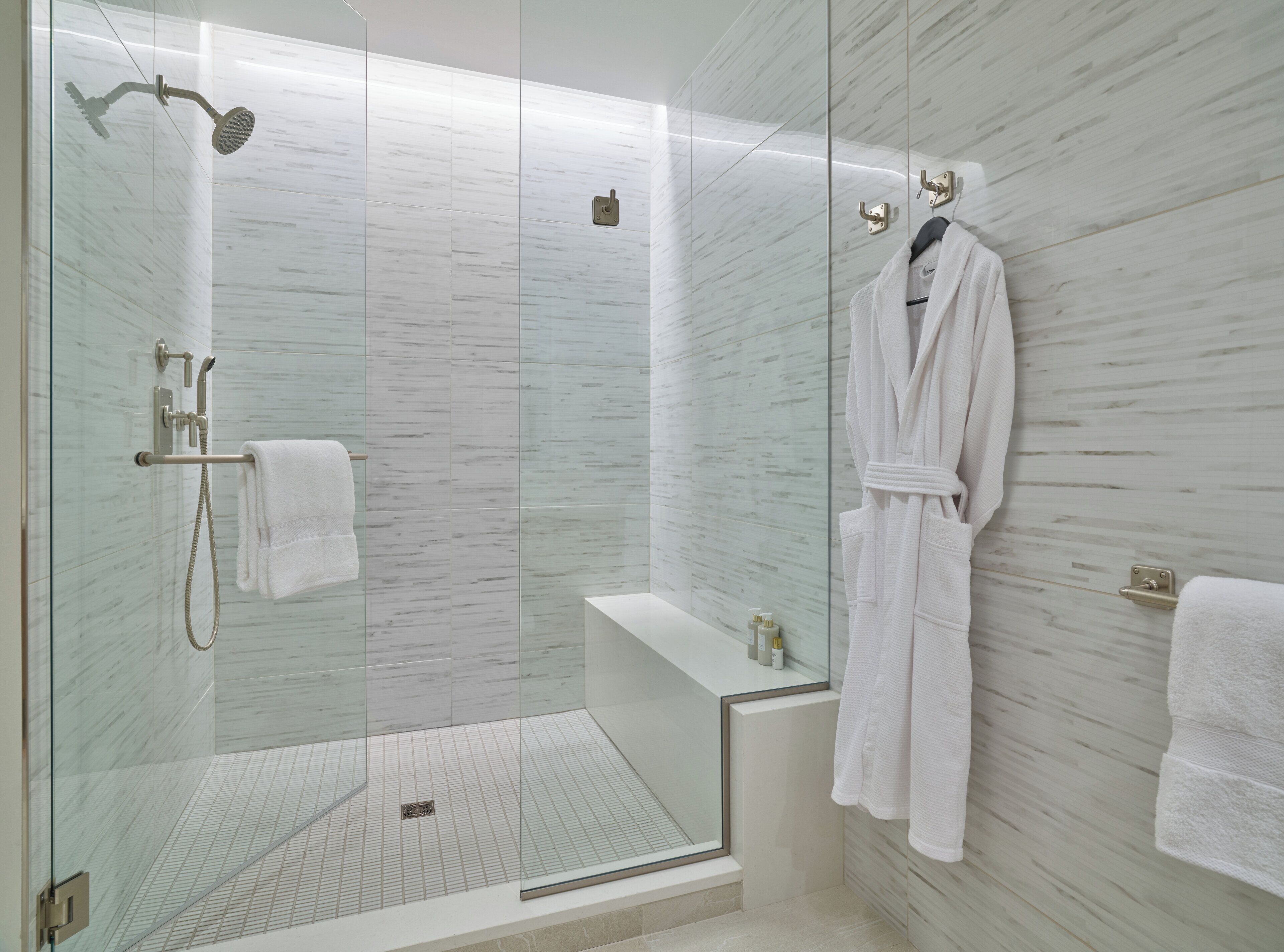 A modern bathroom with a glass-enclosed shower, a bathtub, and a robe hanging on a hook.