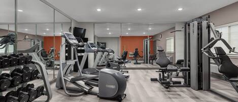 A modern gym with cardio machines, weightlifting equipment, and a mirrored wall.