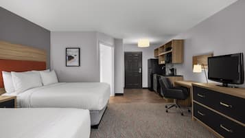 Habitación de hotel con dos camas, un escritorio con computadora, televisor y kitchenette.