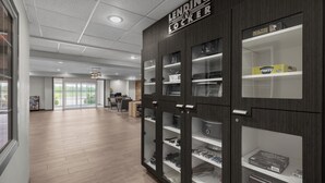 A modern hotel lobby with a wooden floor, a large LENDING LOCKER cabinet, and a view of the outdoors through large windows. - Candlewood Suites Hotel Texas City by IHG (Texas City)