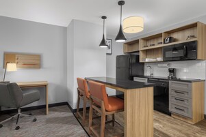 A modern kitchen with a wooden countertop, two pendant lights, a refrigerator, microwave, and a coffee maker.
