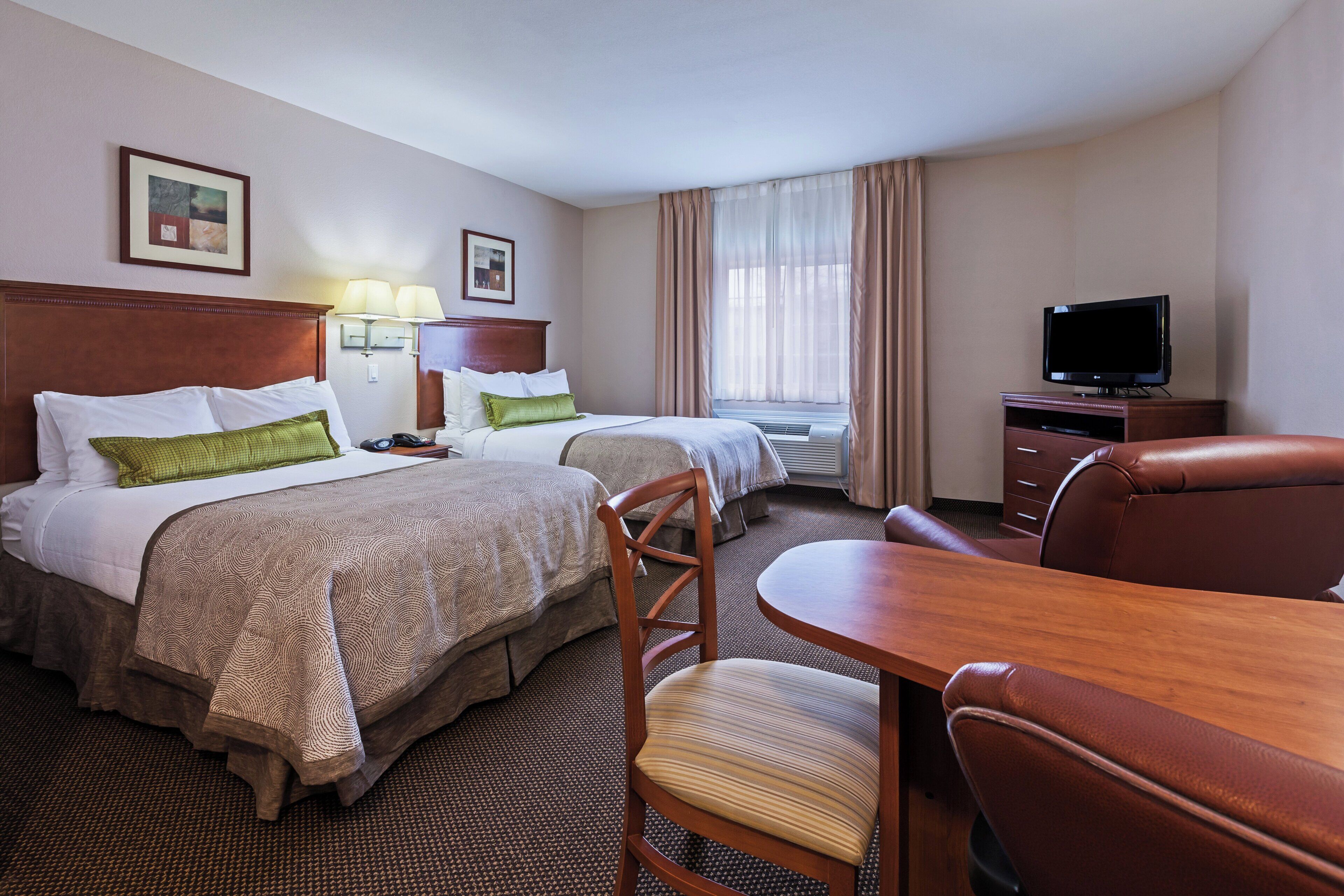 A hotel room with two beds, a desk, a chair, a television, and a window with curtains.