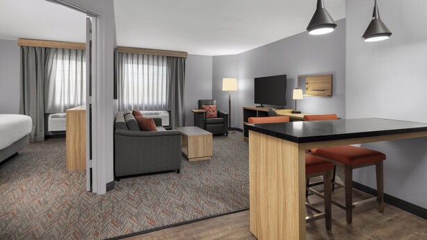 A modern hotel room with a sofa, a small table, a TV, and a kitchenette area. - Candlewood Suites Hotel Texas City by IHG (Texas City)