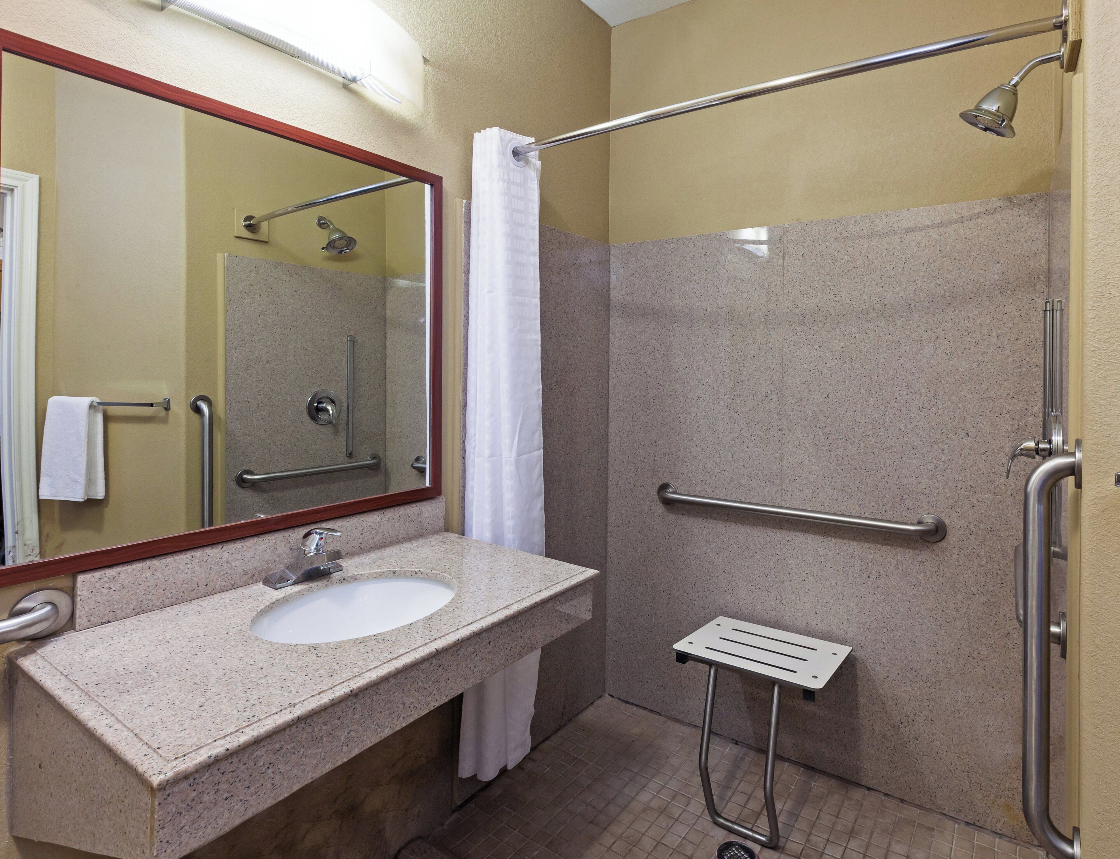 A bathroom with a sink, mirror, shower, and grab bars.
