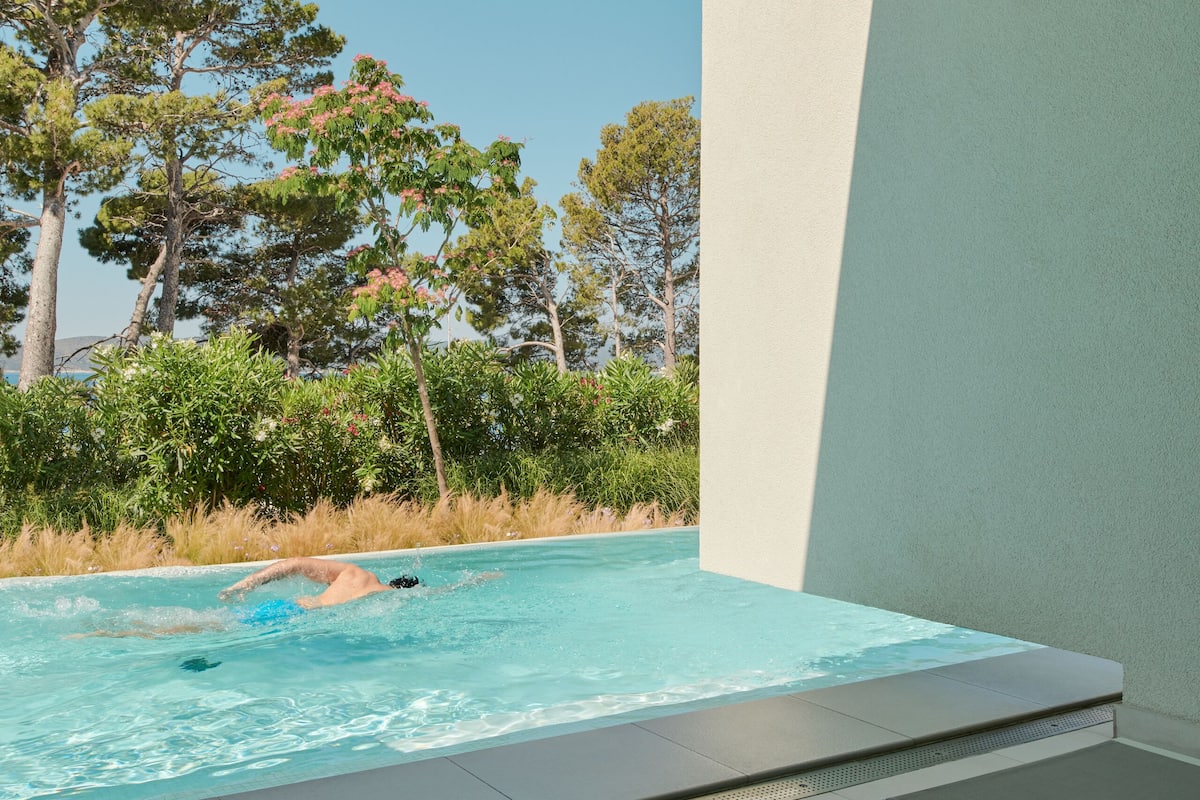 A poolside area with a view of trees, a magazine, and two glasses on a table.