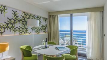 Una habitación moderna con una mesa redonda, sillas verdes, una botella de vino y vistas al océano.