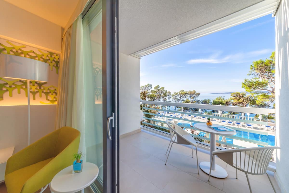 A balcony with a pool view, a chair, a small table, and a potted plant.