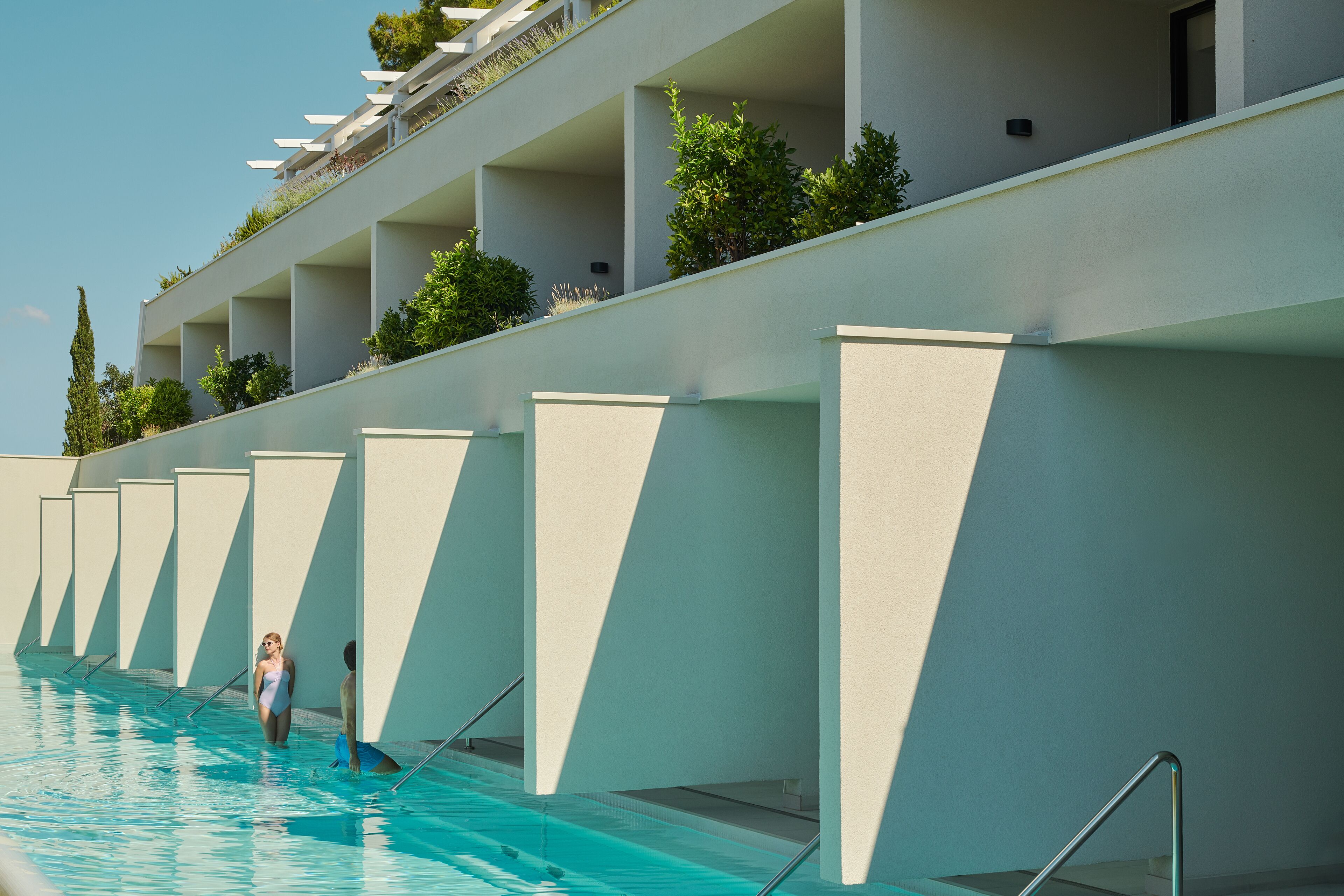 A swimming pool with a modern architectural design, featuring a series of balconies with plants and a clear sky.