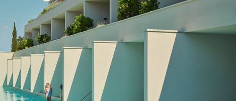 A swimming pool with a modern architectural design, featuring a series of balconies with plants and a clear sky.