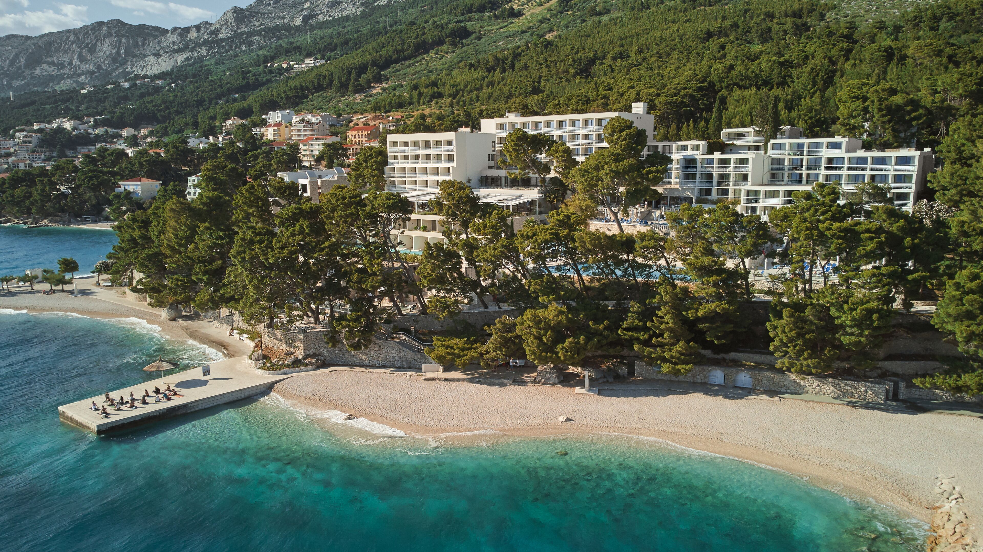 A coastal hotel with multiple buildings, a beach, and a pier.