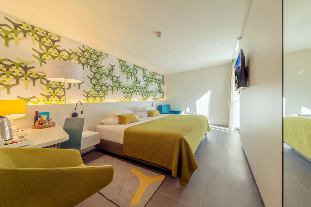 A modern hotel room with a bed, bedside table, lamp, chair, and a decorative wall.