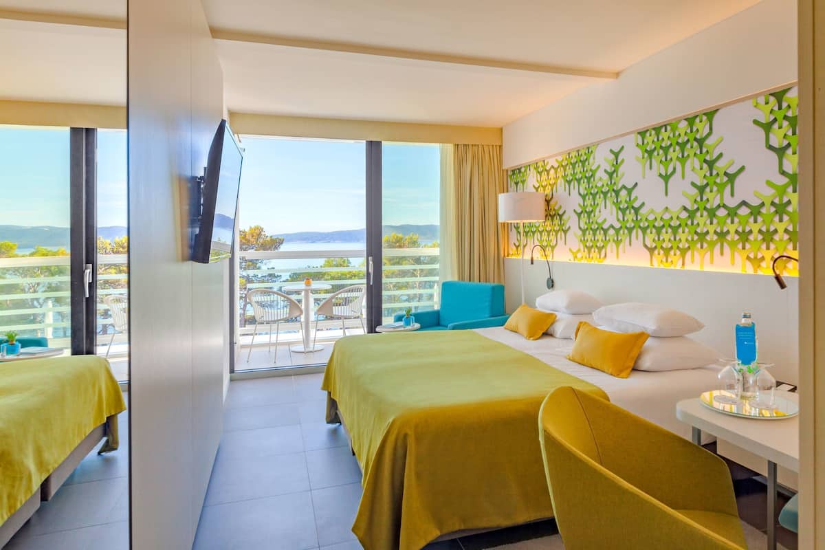 A hotel room with two beds, a balcony with a view, a decorative wall, and a small table with a bottle.
