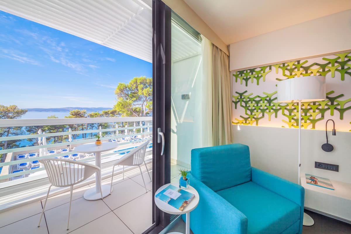 A balcony with a view of the sea, a blue sofa, a small table with a plant, and a white chair.