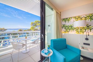 Un balcón con vista al mar, un sofá azul, una mesita con una planta y una silla blanca.