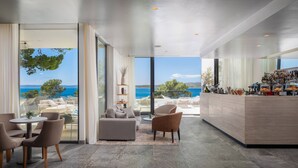 A modern interior with a bar area and seating by a large window overlooking the sea.