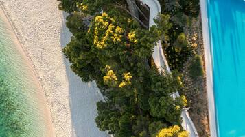 An aerial view of a beach with clear turquoise water, white sand, and dense green trees.