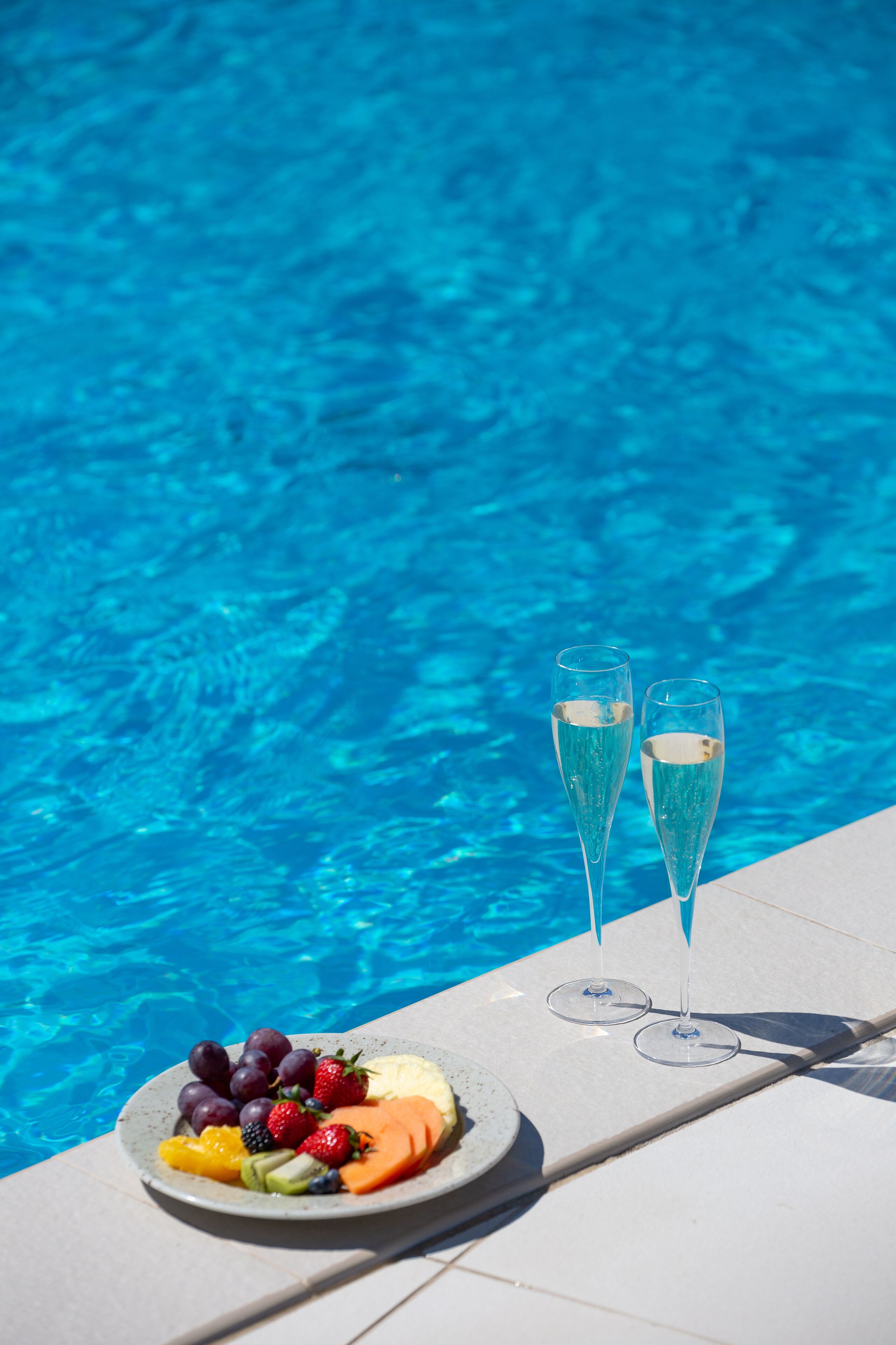 Une scène au bord de la piscine, avec une assiette de fruits et deux coupes à champagne.