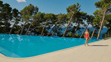Zona de piscina con vista despejada al mar y árboles al fondo.