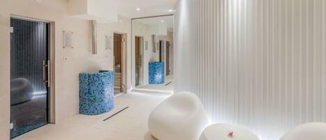 A modern hotel lobby with a minimalist design, featuring a large mirror, a blue mosaic column, and white seating areas.