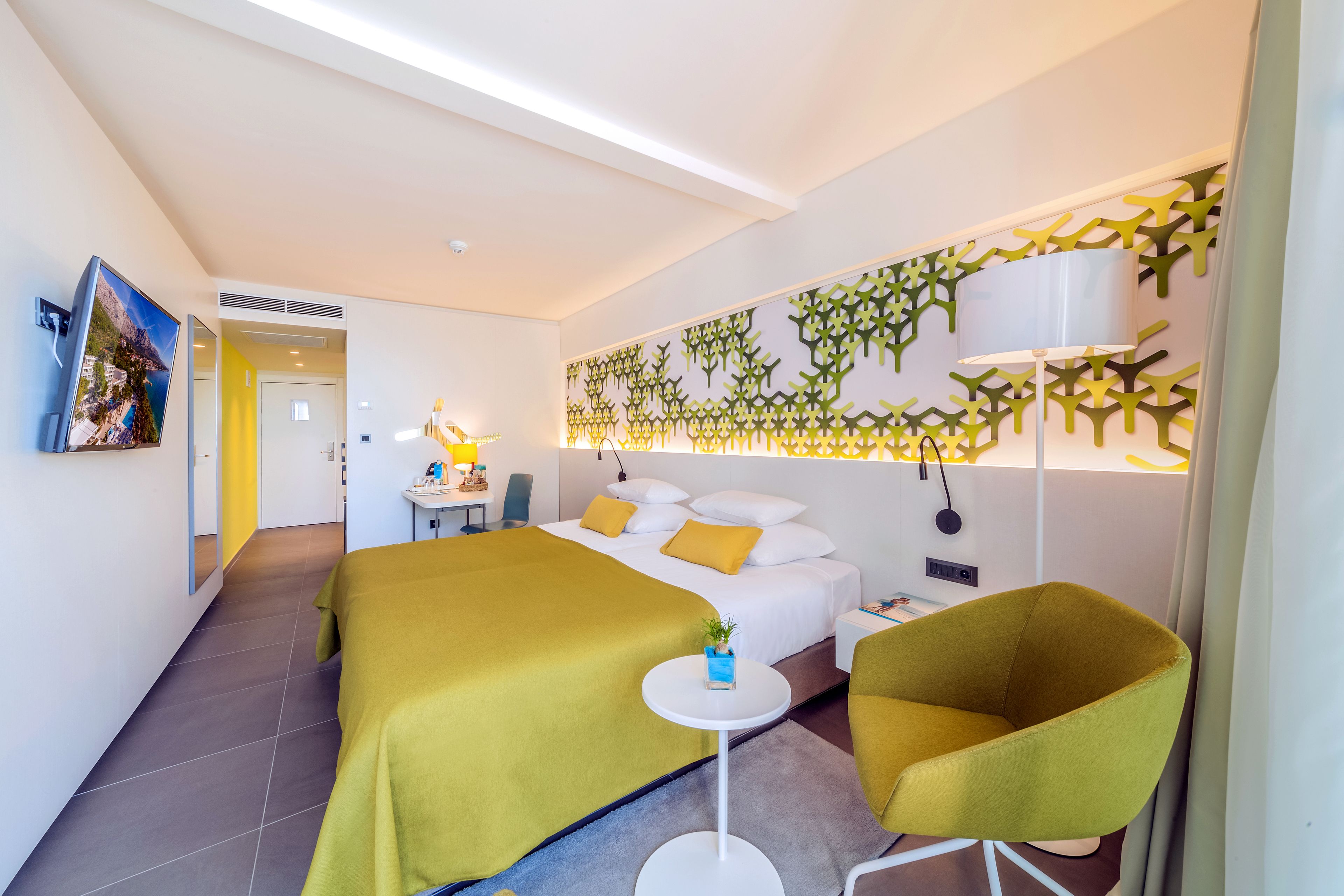 Una camera d'albergo moderna con un letto, un tavolino, una sedia e un pannello decorativo a parete.