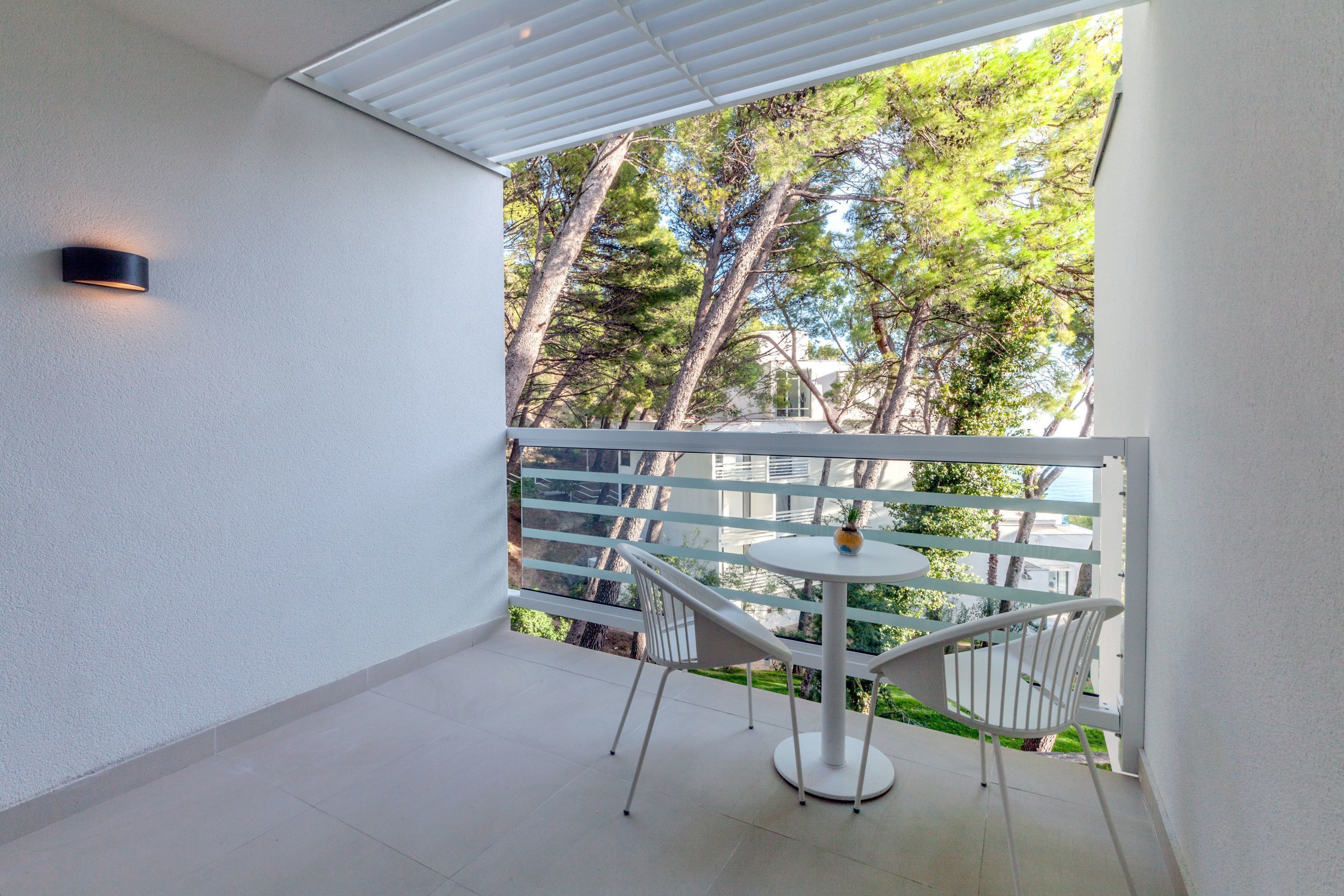 Een balkon met een witte hekwerk, een kleine ronde tafel en twee witte stoelen.