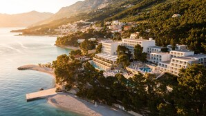 A coastal hotel with multiple buildings, a beach, and a mountain backdrop.