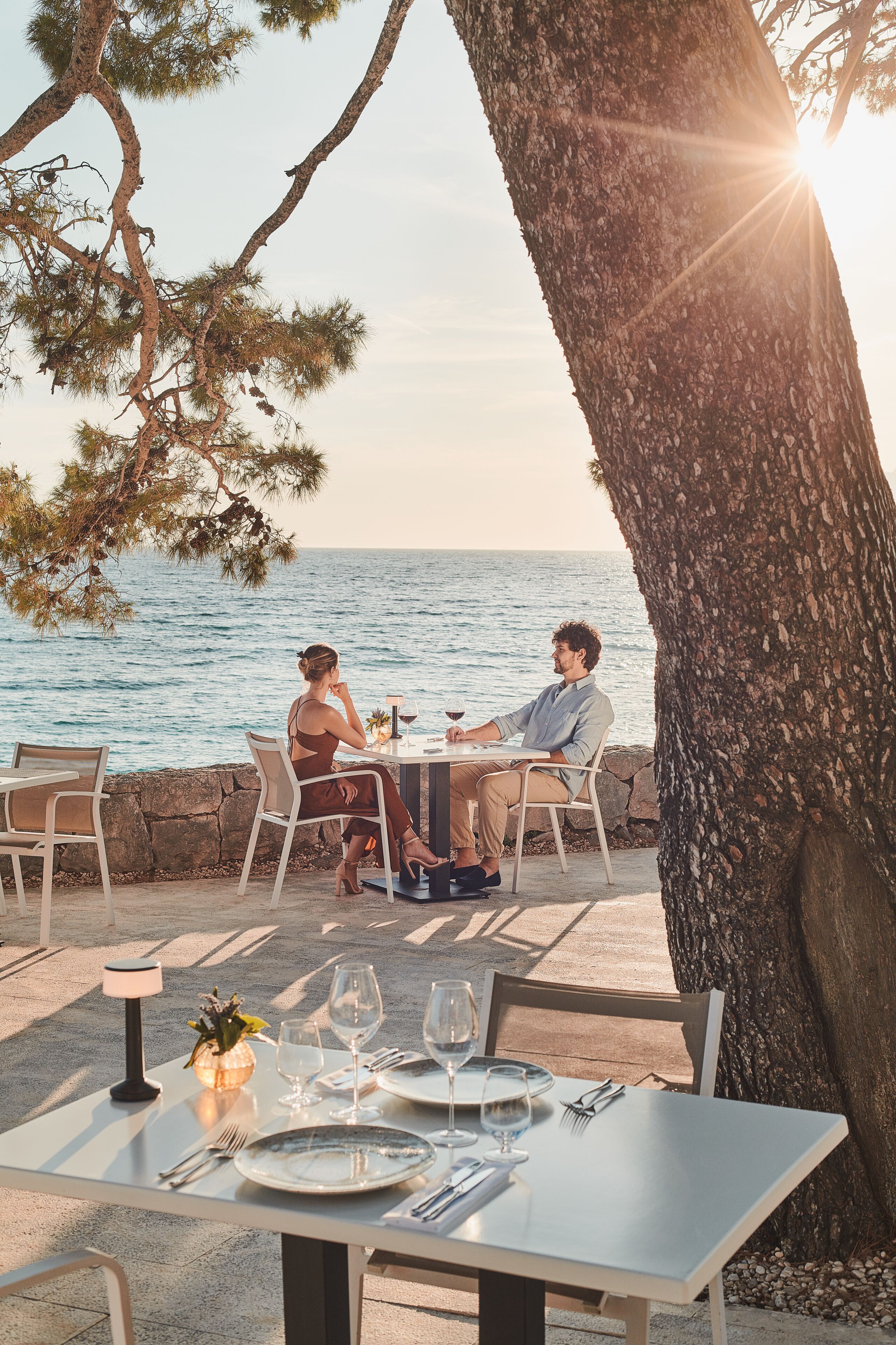 Mesa para dos con vistas al mar, un árbol y una lámpara.