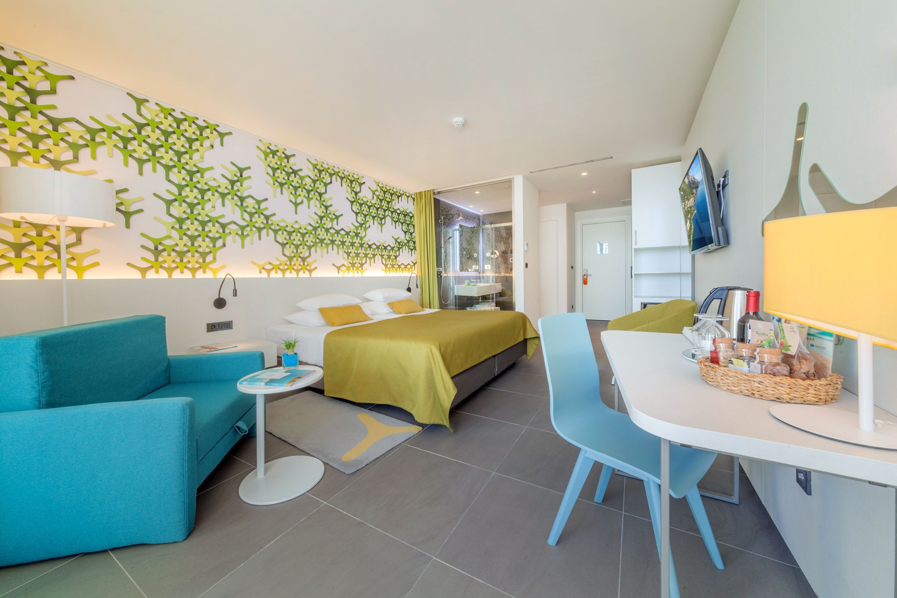 A modern hotel room with a bed, a sofa, a desk, and a TV.
