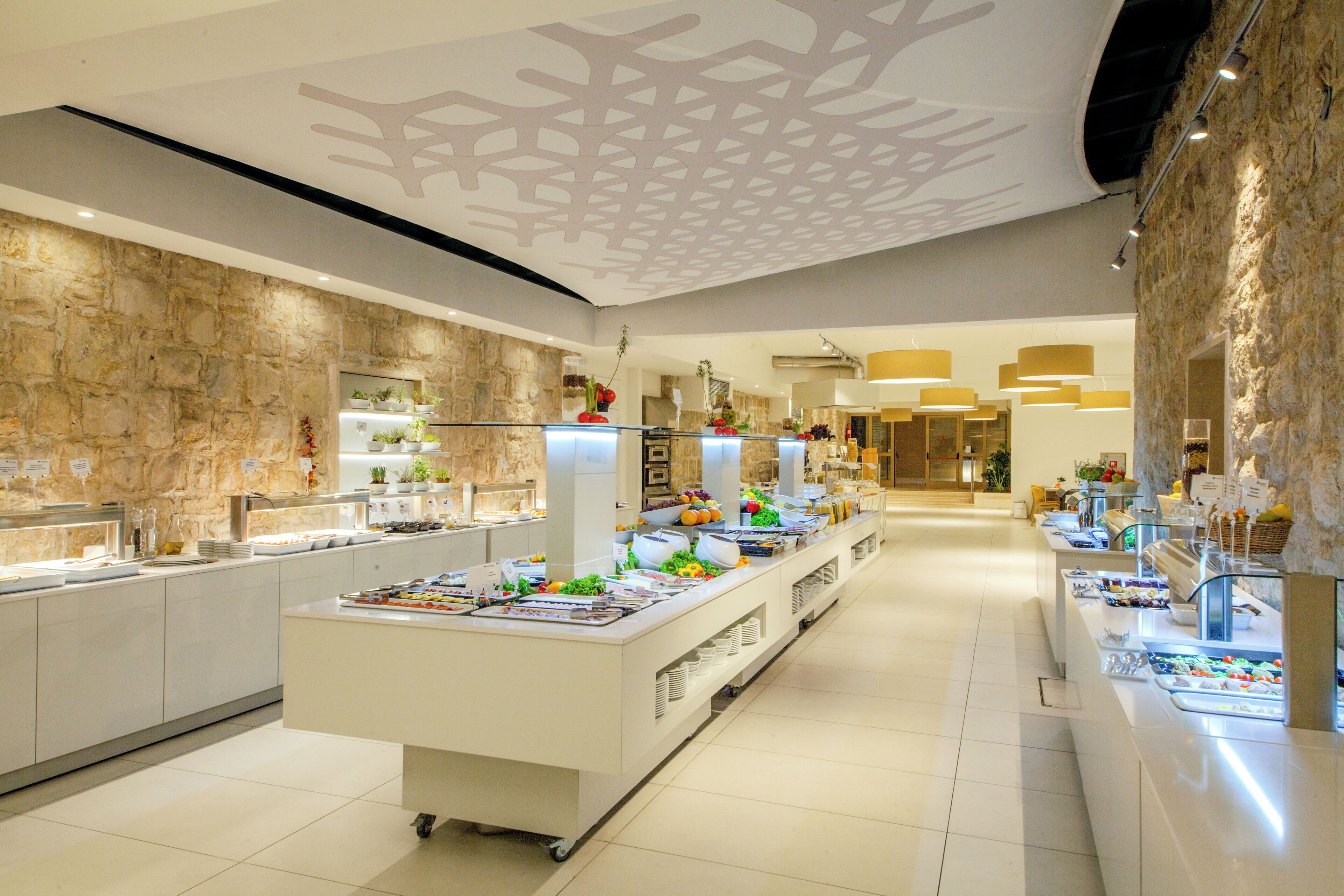 Un moderno vestíbulo de hotel con zona de buffet central, detalles en pared de piedra e iluminación contemporánea.