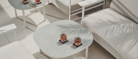 Un área de estar moderna al aire libre con dos mesas redondas, cada una con una copa de bebida de color ámbar y una revista.