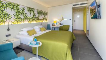 A modern hotel room with a large bed, a desk, a chair, a TV, and a decorative wall.