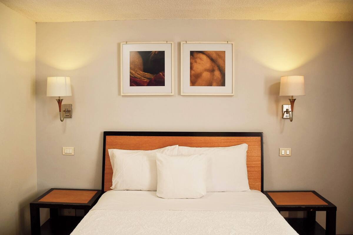 A hotel room with a bed, two nightstands, two wall-mounted lamps, and two framed pictures on the wall.