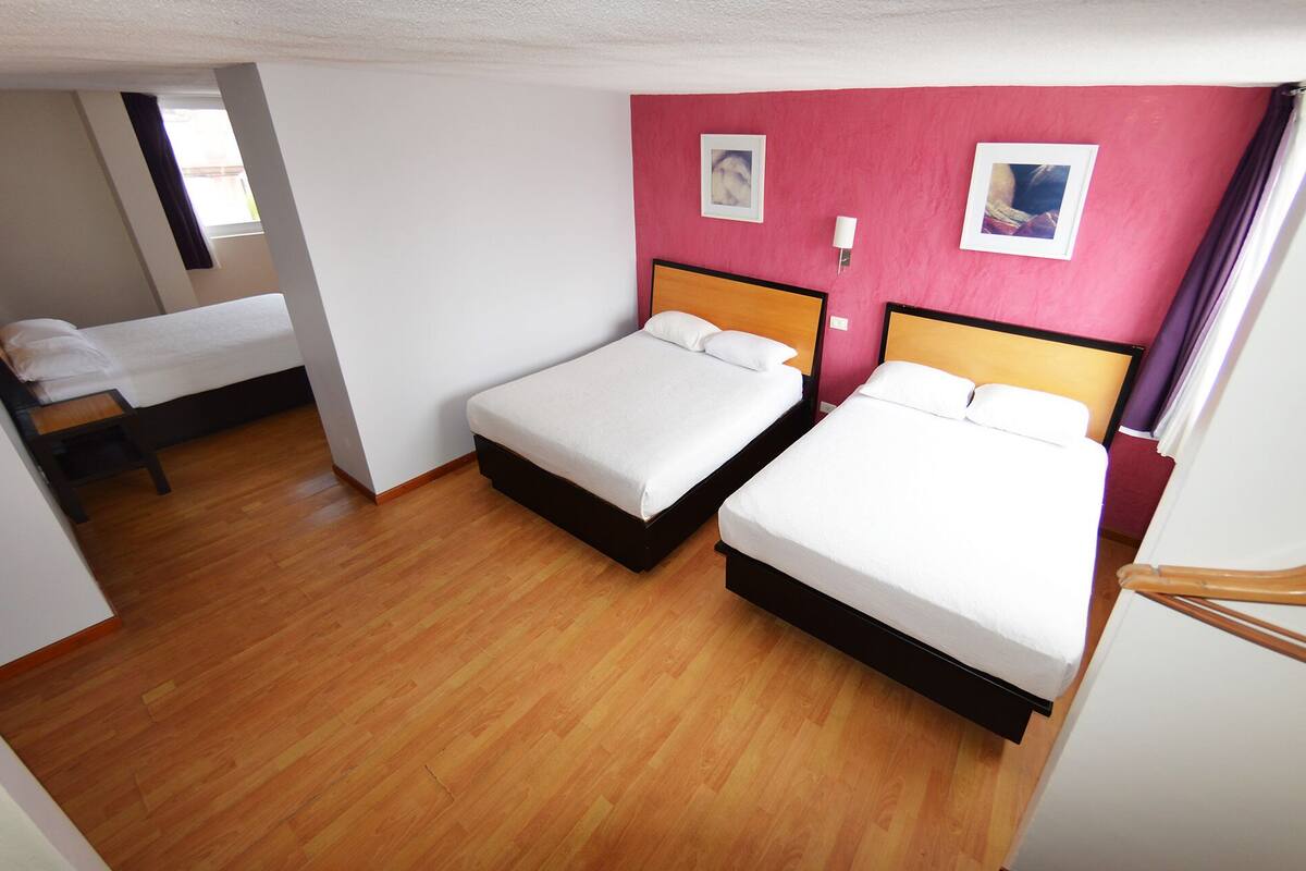 A hotel room with two single beds, wooden flooring, a small table, and a window.