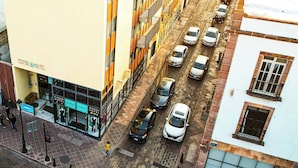 A hotel with a modern facade, multiple floors, and a parking area with several cars. - Centro 19 Hotel (Querétaro)