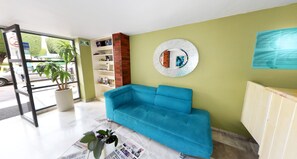 A room with a blue sofa, a round mirror on the wall, a bookshelf, and a potted plant. - Centro 19 Hotel (Querétaro)