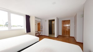 A hotel room with two beds, a window with curtains, a wooden door, and a small seating area with a chair. - Centro 19 Hotel (Querétaro)