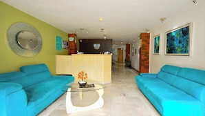 A hotel lobby with two blue sofas, a glass coffee table, a reception desk, and a mirror on the wall. - Centro 19 Hotel (Querétaro)
