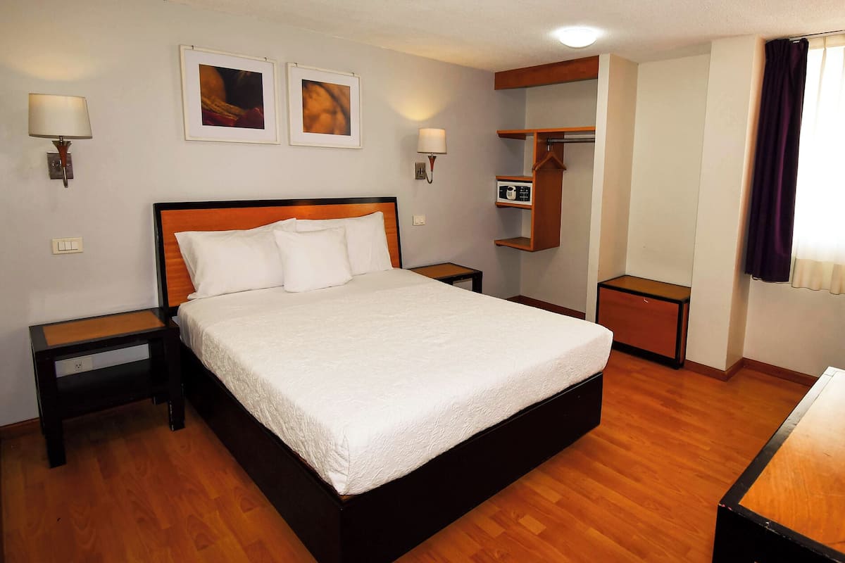 A neatly arranged hotel room with a large bed, bedside tables, a wardrobe, and a desk.