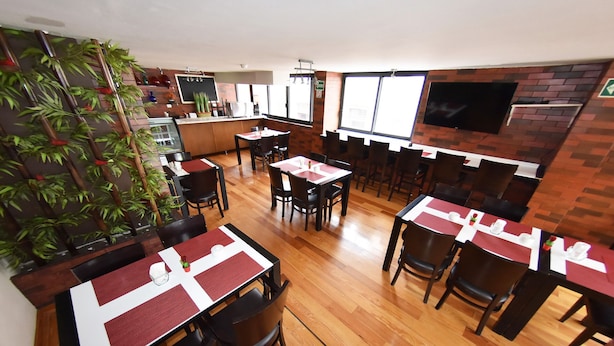 A restaurant with wooden flooring, multiple tables with red placemats, black chairs, and a brick wall with a TV mounted above. - Centro 19 Hotel (Querétaro)