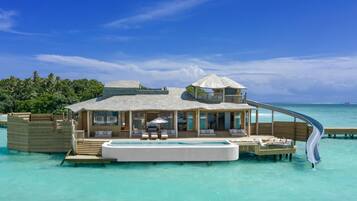 A luxurious overwater bungalow with a private pool, a slide, and a thatched-roof structure.